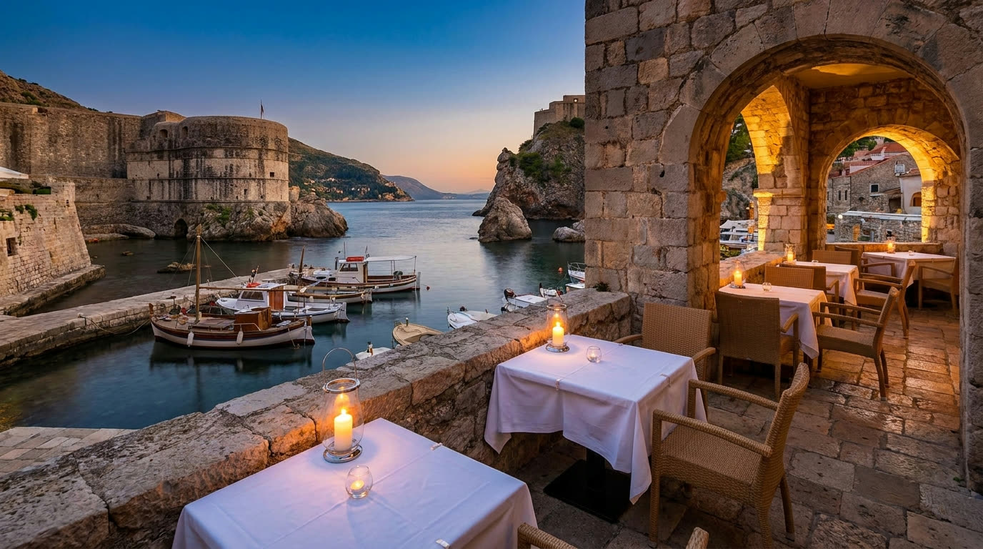 Fine-dining terrace set against fortress walls beside Dubrovnik's old harbour at dusk