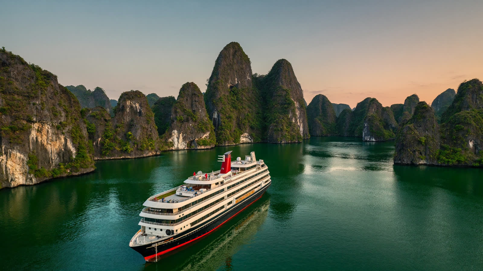 Luxury junk cruise among Ha Long Bay limestone karsts at sunset