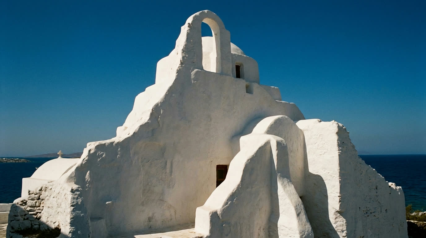 The asymmetric whitewashed mass of Panagia Paraportiani church against blue sky in Mykonos